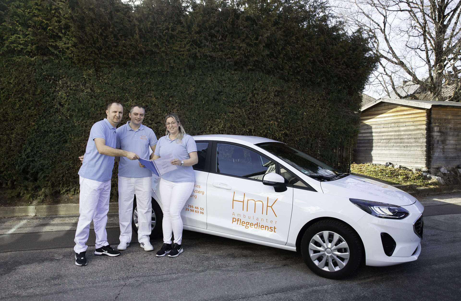 Pflegedienst HmK mit Team vor Fahrzeug, mobile Pflege in Aktion.